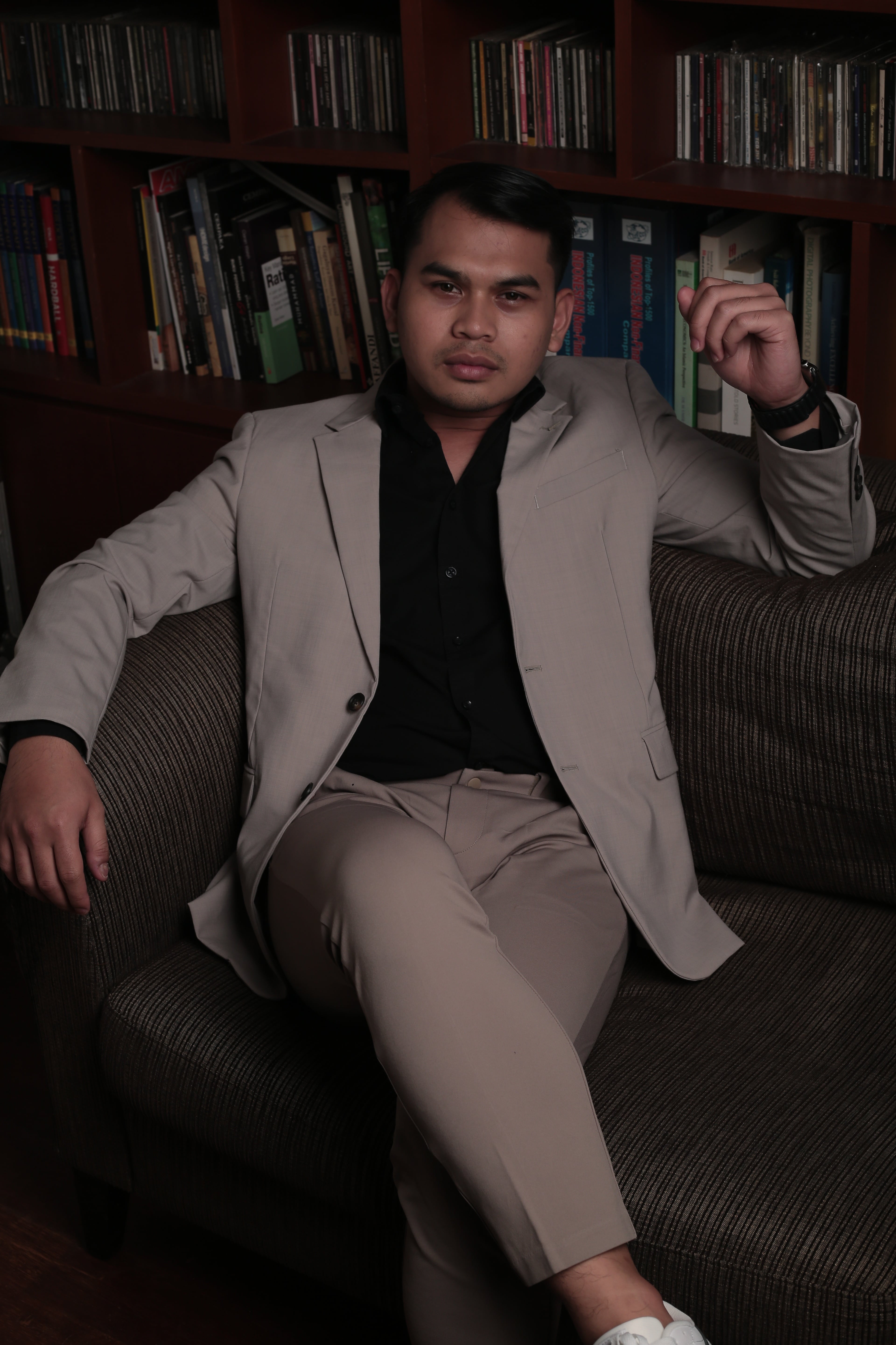 Hida Aldric seated in a library wearing a suit